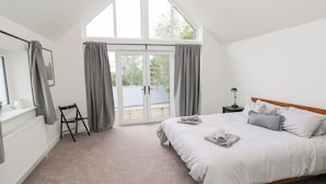 A bedroom with a large bed, a nightstand, a chair, and a view through a sliding glass door to the outside.