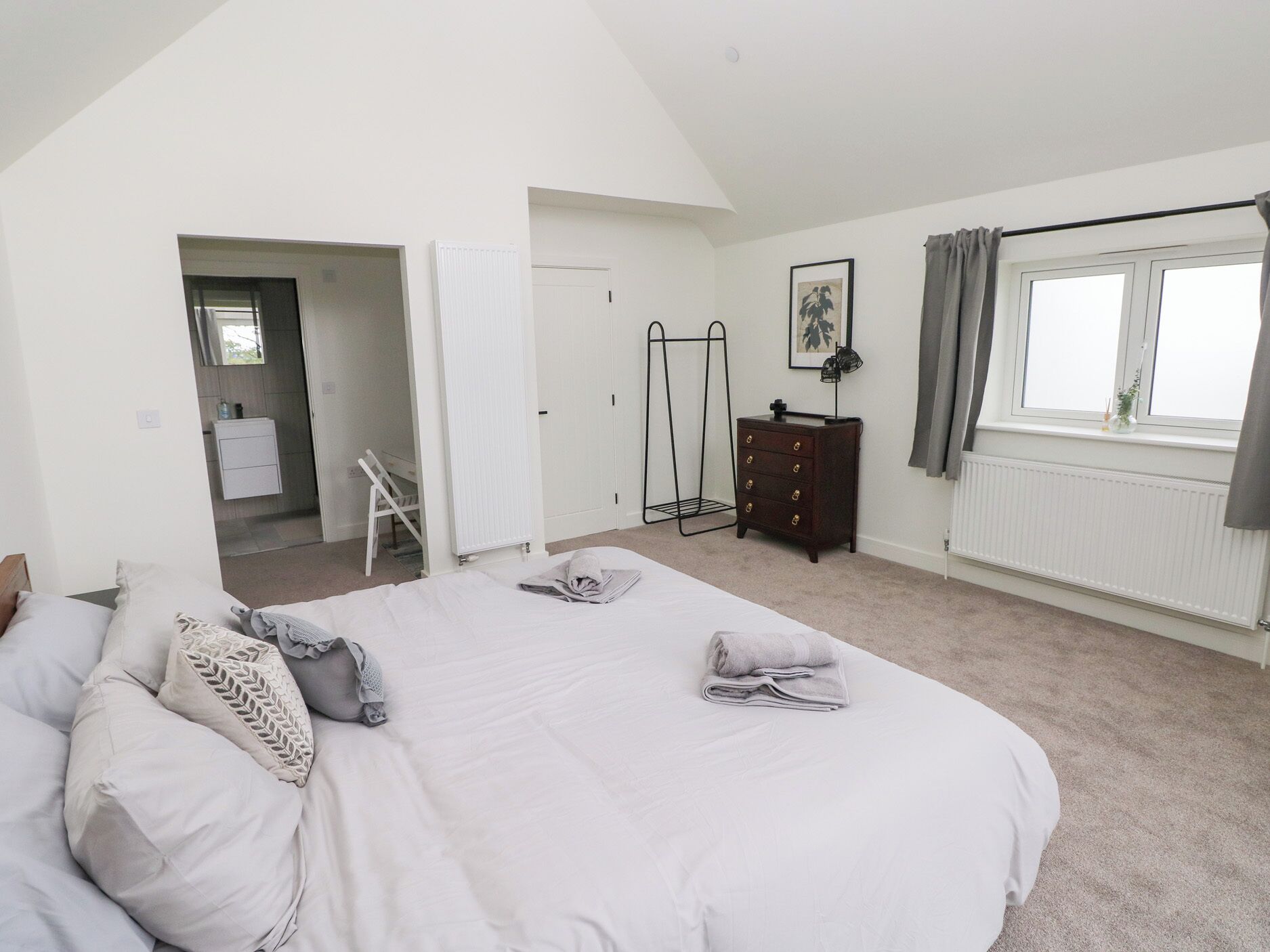 A bedroom with a large bed, a dresser, a radiator, and a window with curtains.