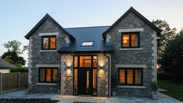 A two-story stone house with a dark roof, a central entrance with glass doors, and two windows on each side.