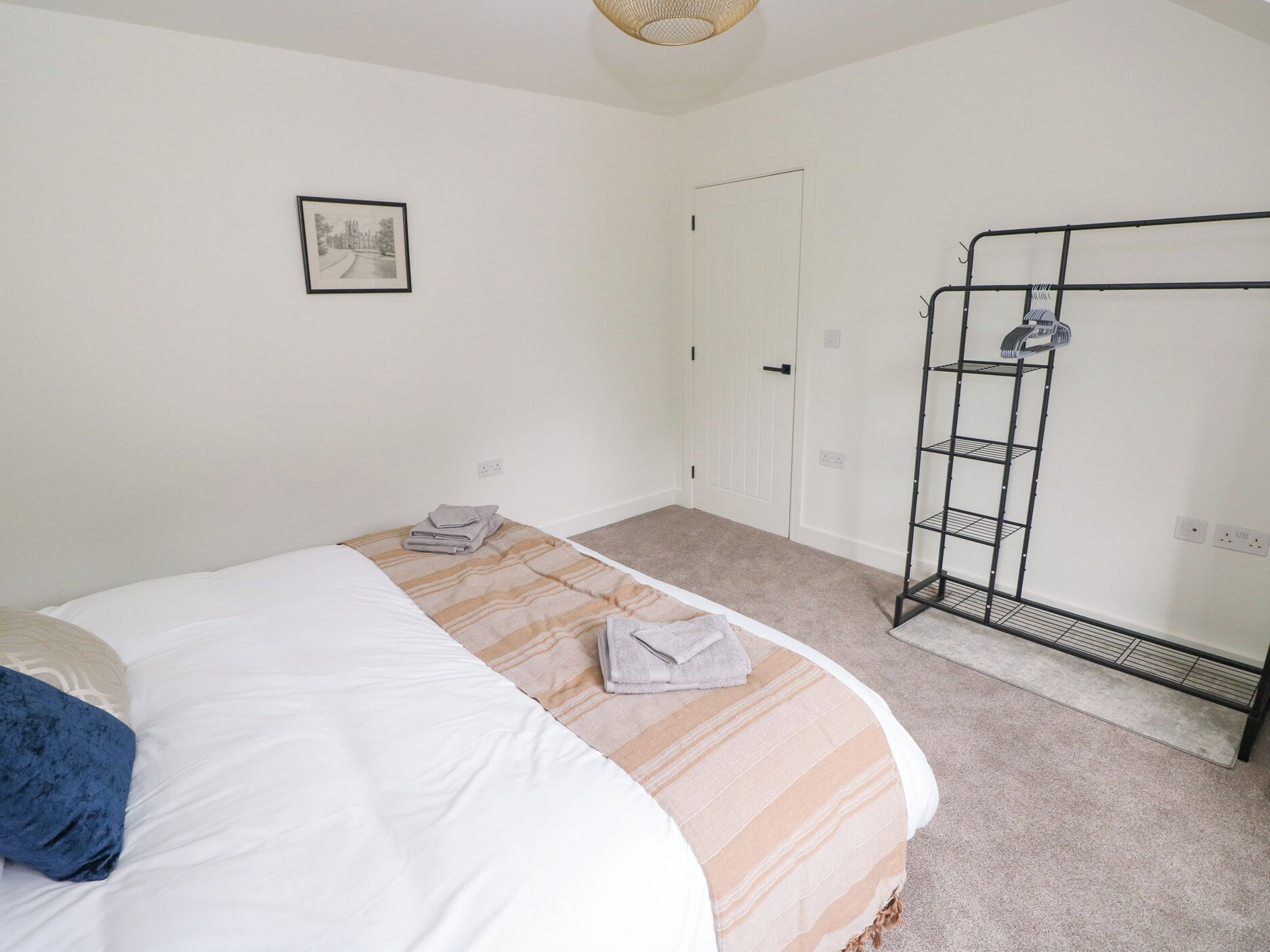 A bedroom with a bed, a wardrobe, a hanging rack, and a framed picture on the wall.