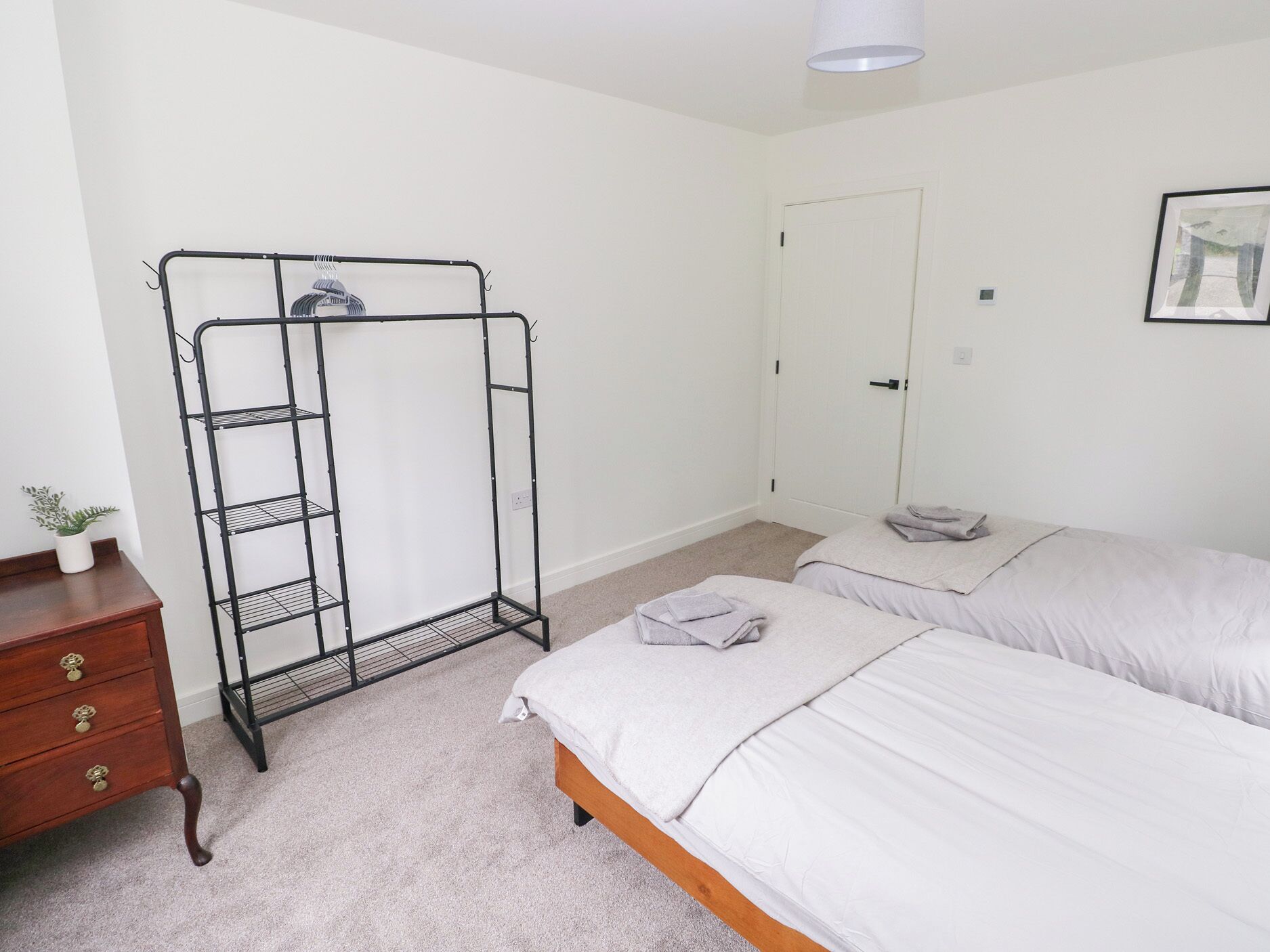 A bedroom with a bed, a wooden dresser, a metal shelving unit, and a door.