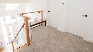 A spacious room with a high ceiling, a glass railing staircase, a white door, and a hanging light fixture.