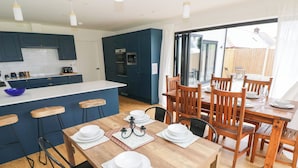 A modern kitchen with blue cabinets, a wooden dining table set with white plates and bowls, and a view of the outdoors through large sliding glass doors.