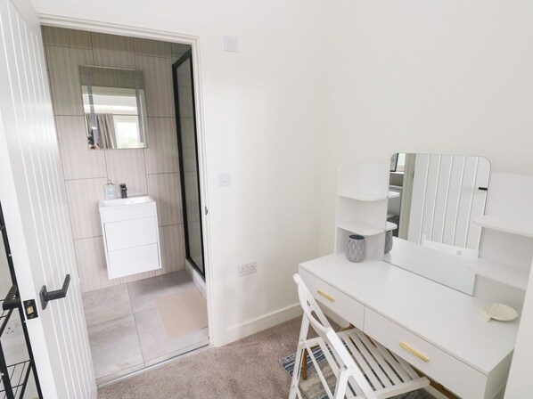 A modern bathroom with a white vanity, a mirror, and a shower area. - Ty Landsker (Milford Haven)
