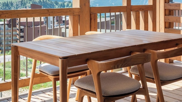 A wooden deck with a table and chairs, overlooking a mountain range.