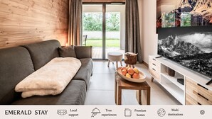 Un salon moderne avec un canapé gris, un buffet en bois et un téléviseur diffusant un paysage de montagne.