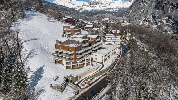 Une station de montagne enneigée, dotée de bâtiments modernes à plusieurs étages, de pistes de ski et offrant une vue dégagée sur les montagnes environnantes.