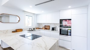 Een moderne keuken met witte kasten, een marmeren aanrecht en een ingebouwde oven.