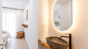 Een moderne badkamer met een grote, ovale spiegel, een stenen wastafel en een houten bijzettafeltje.