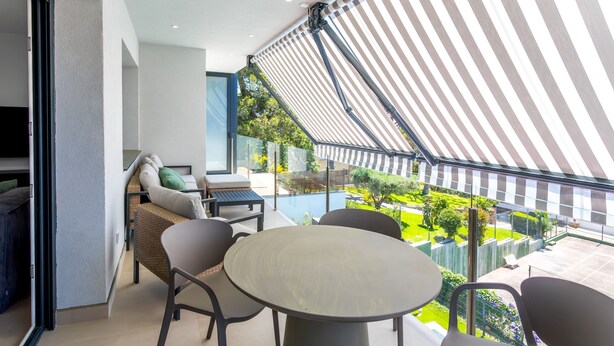 Ein Balkon mit rundem Tisch und Stühlen, einer Couch und einem Fernseher.