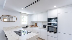 Eine moderne Küche mit weißen Schränken, einer Marmorarbeitsplatte und eingebauten Geräten, darunter ein Herd und ein Backofen.