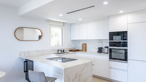 Une cuisine moderne avec des meubles blancs, un plan de travail en marbre, un four encastré et une grande fenêtre.