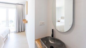 Une chambre d’hôtel moderne avec un grand lit, un miroir rond, une table de chevet en bois et un lavabo intégré.