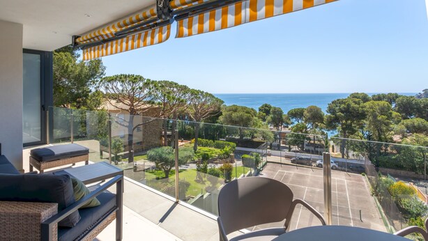 Un balcon avec vue sur la mer, des meubles d’extérieur et une rambarde en verre.