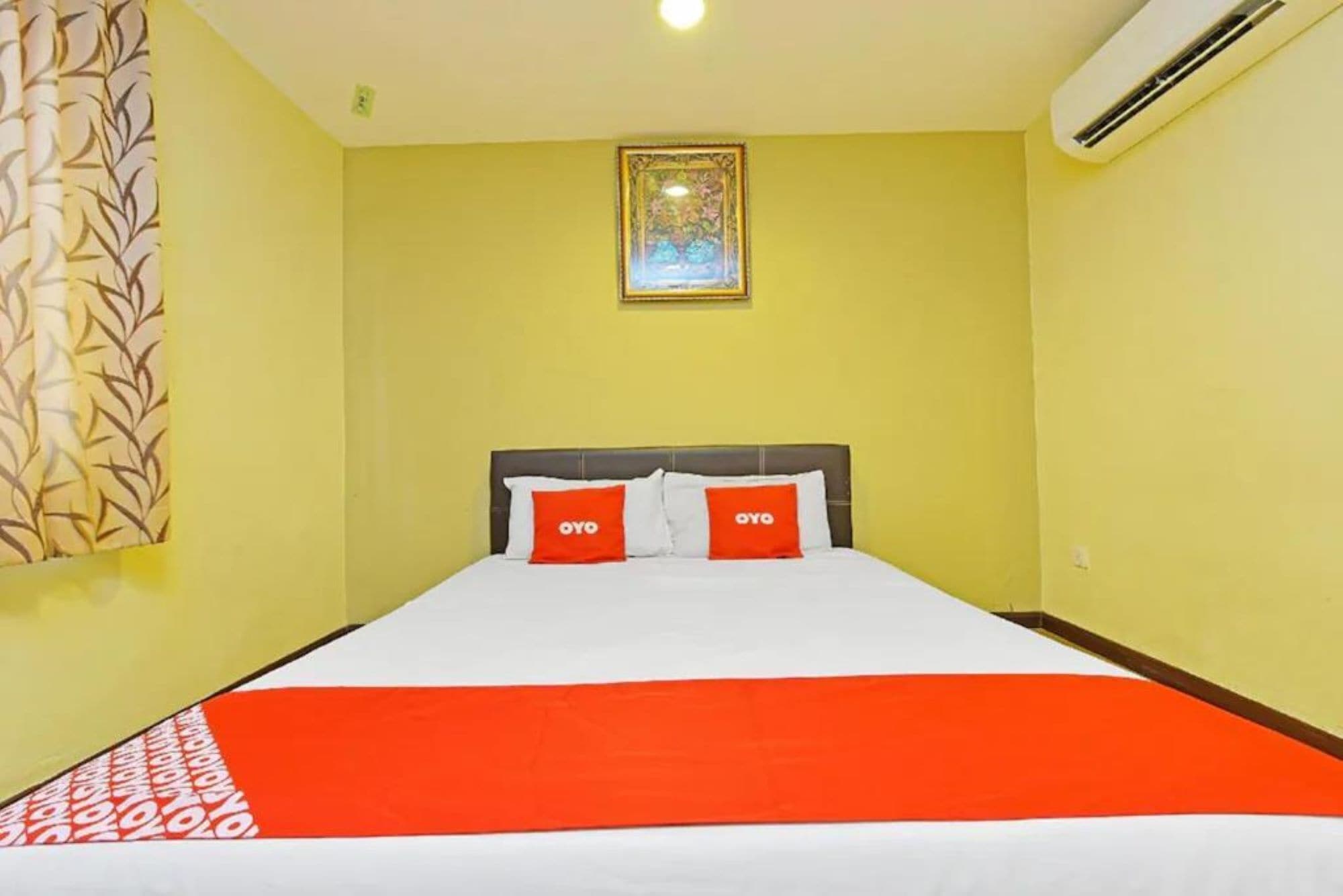 Habitación de hotel con cama, cabecera, aire acondicionado fijado a la pared y un cuadro enmarcado sobre la cama.