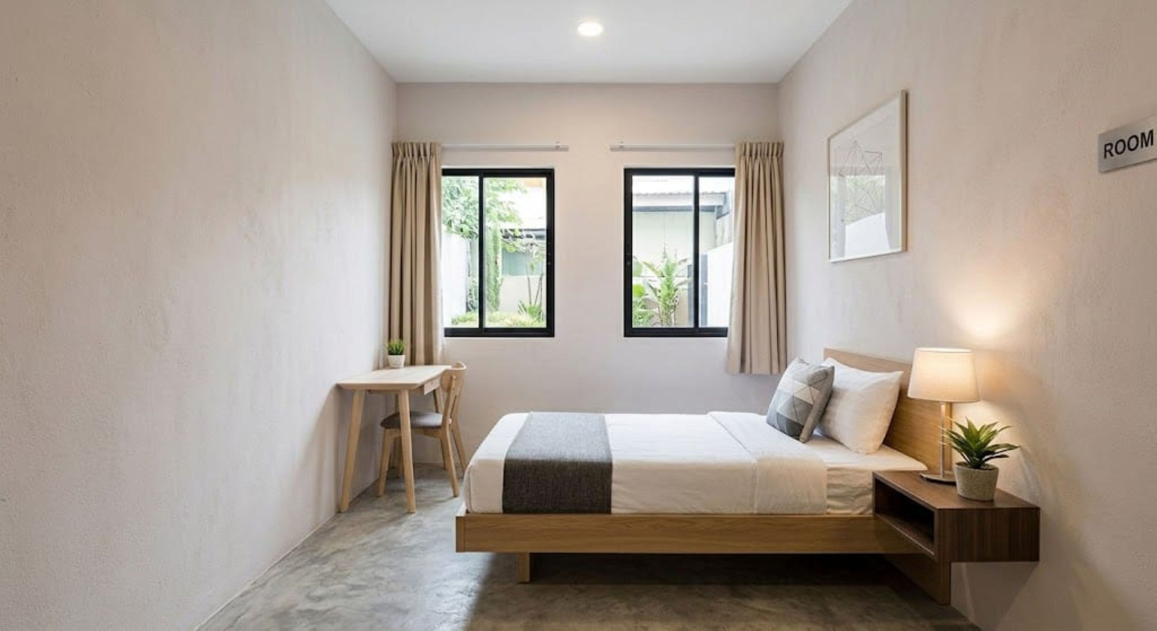 A bedroom with a bed, bedside table, lamp, and a desk with chair.