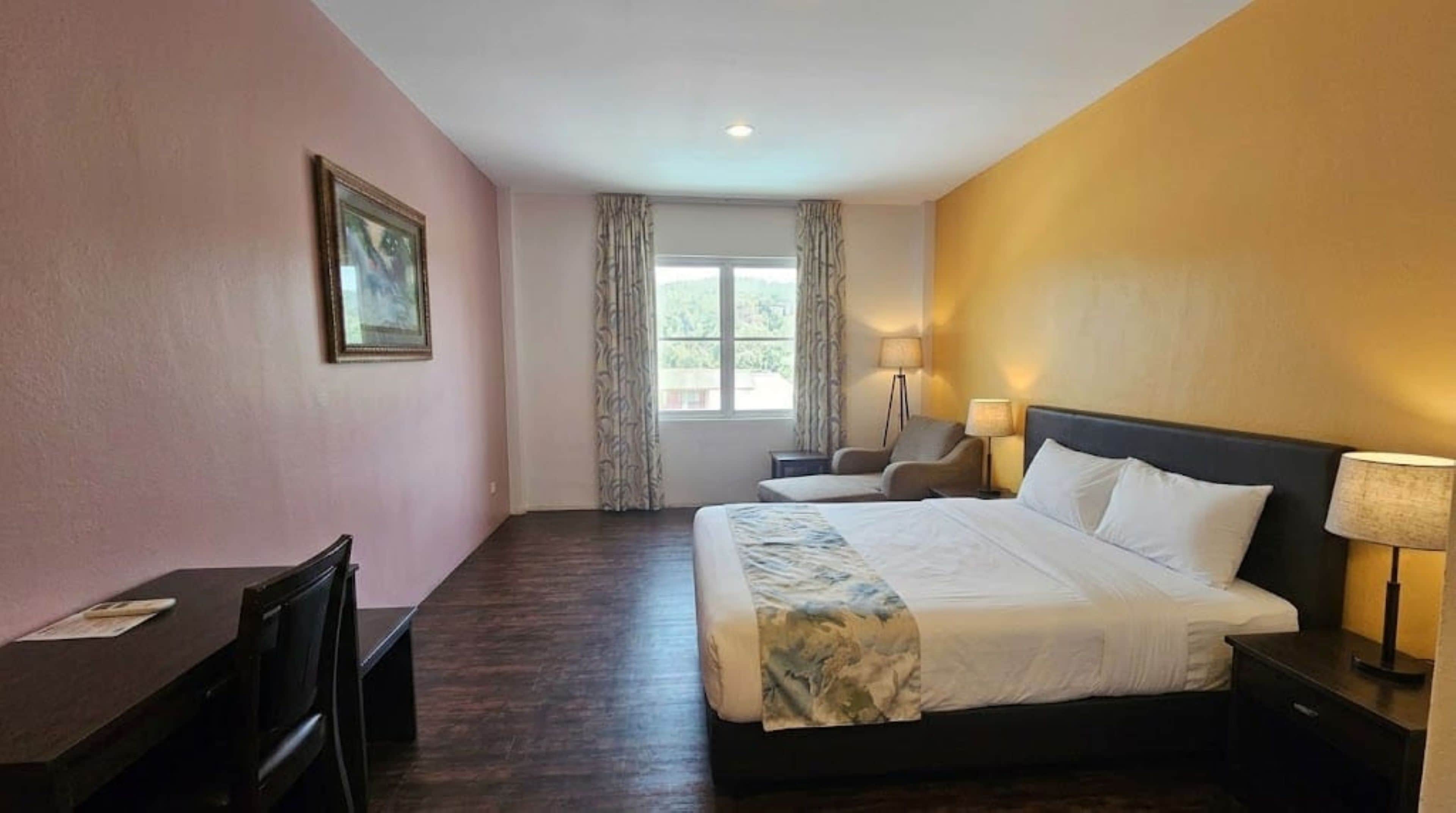 A hotel room with a bed, desk, chair, and a window with curtains.