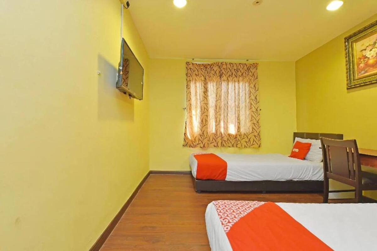 A room with two beds, a wooden floor, a window with patterned curtains, and a painting on the wall.