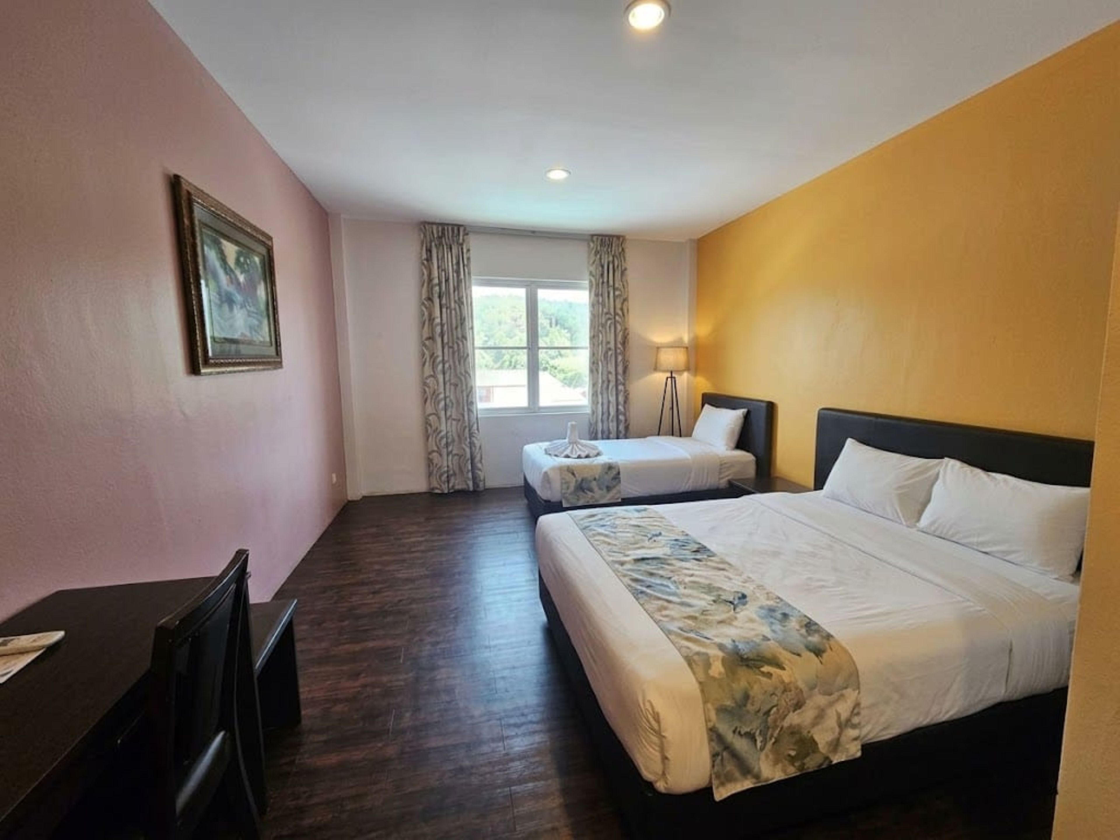 A hotel room with two beds, a desk, and a window with curtains.