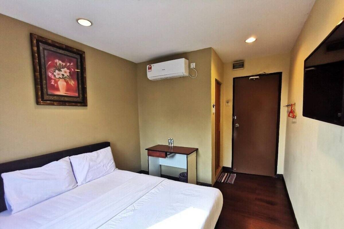A hotel room with a bed, a small desk, an air conditioning unit, and a door.