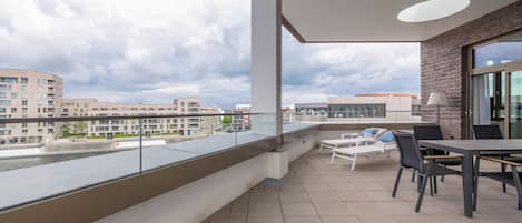 Un balcon donnant sur des immeubles, une table avec des chaises et une lampe.