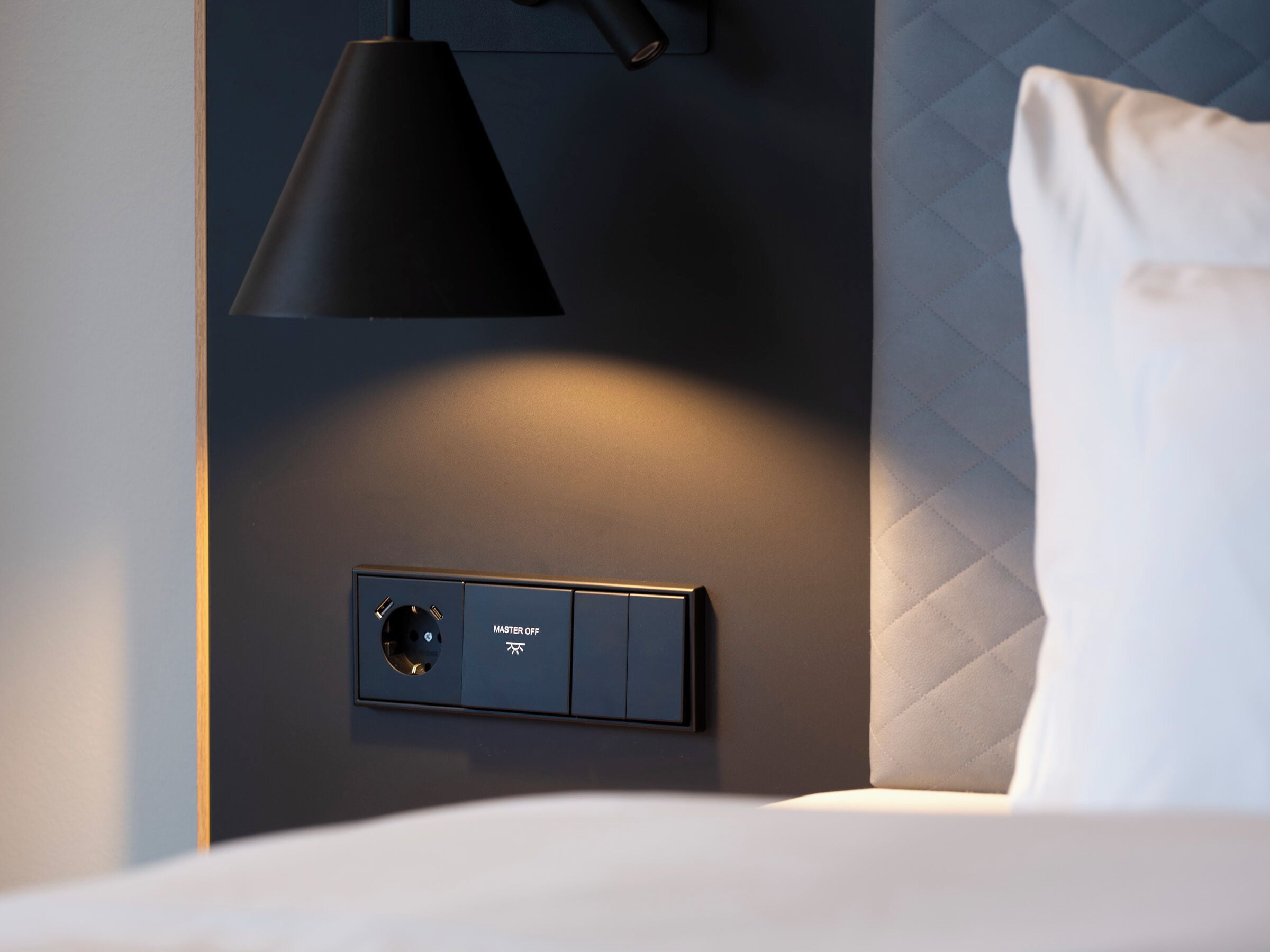 A modern room with a bed, a wall-mounted control panel, and a pendant light.