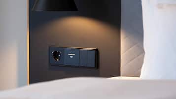 A modern room with a bed, a wall-mounted control panel, and a pendant light.