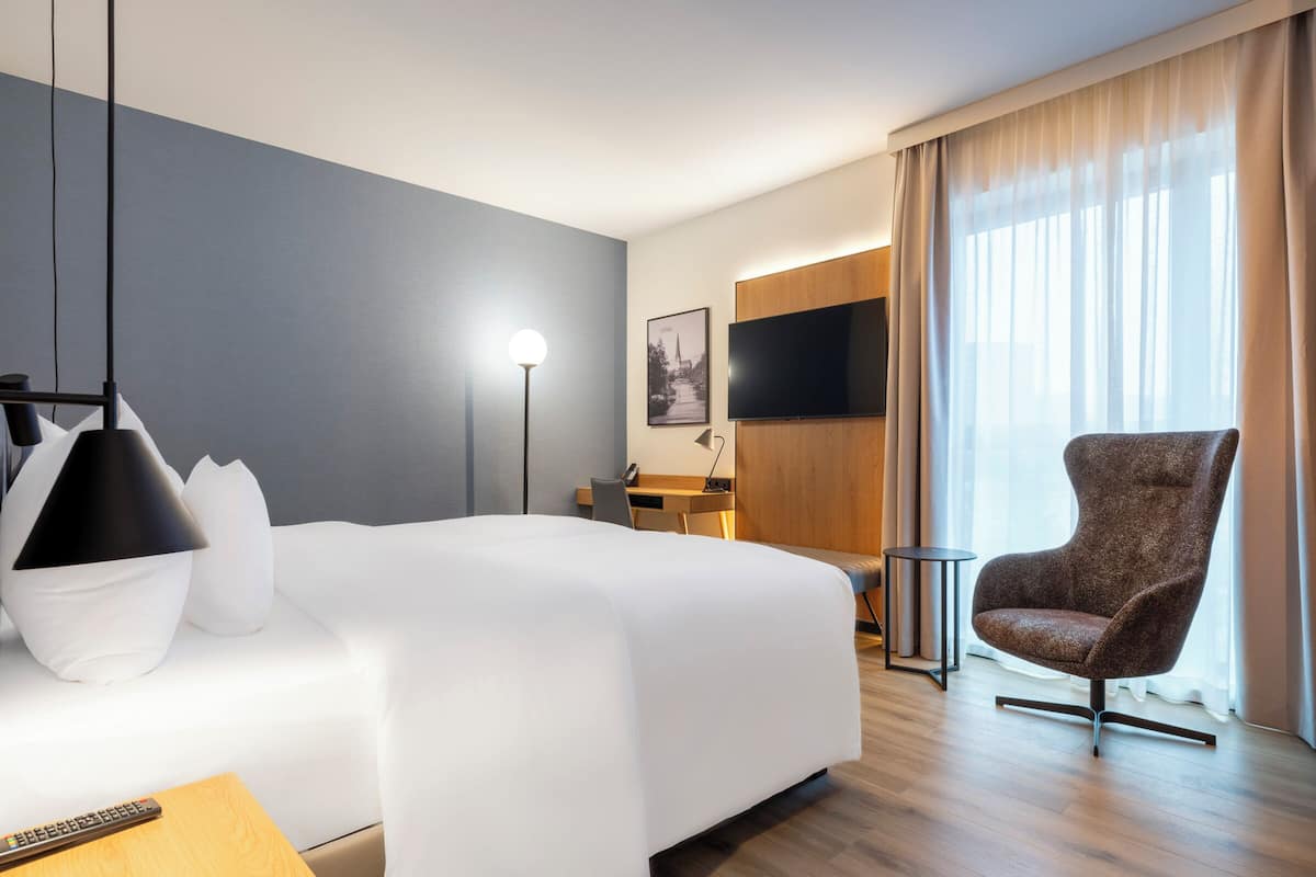 A hotel room with a large bed, a desk, a chair, a TV, and a window with curtains.