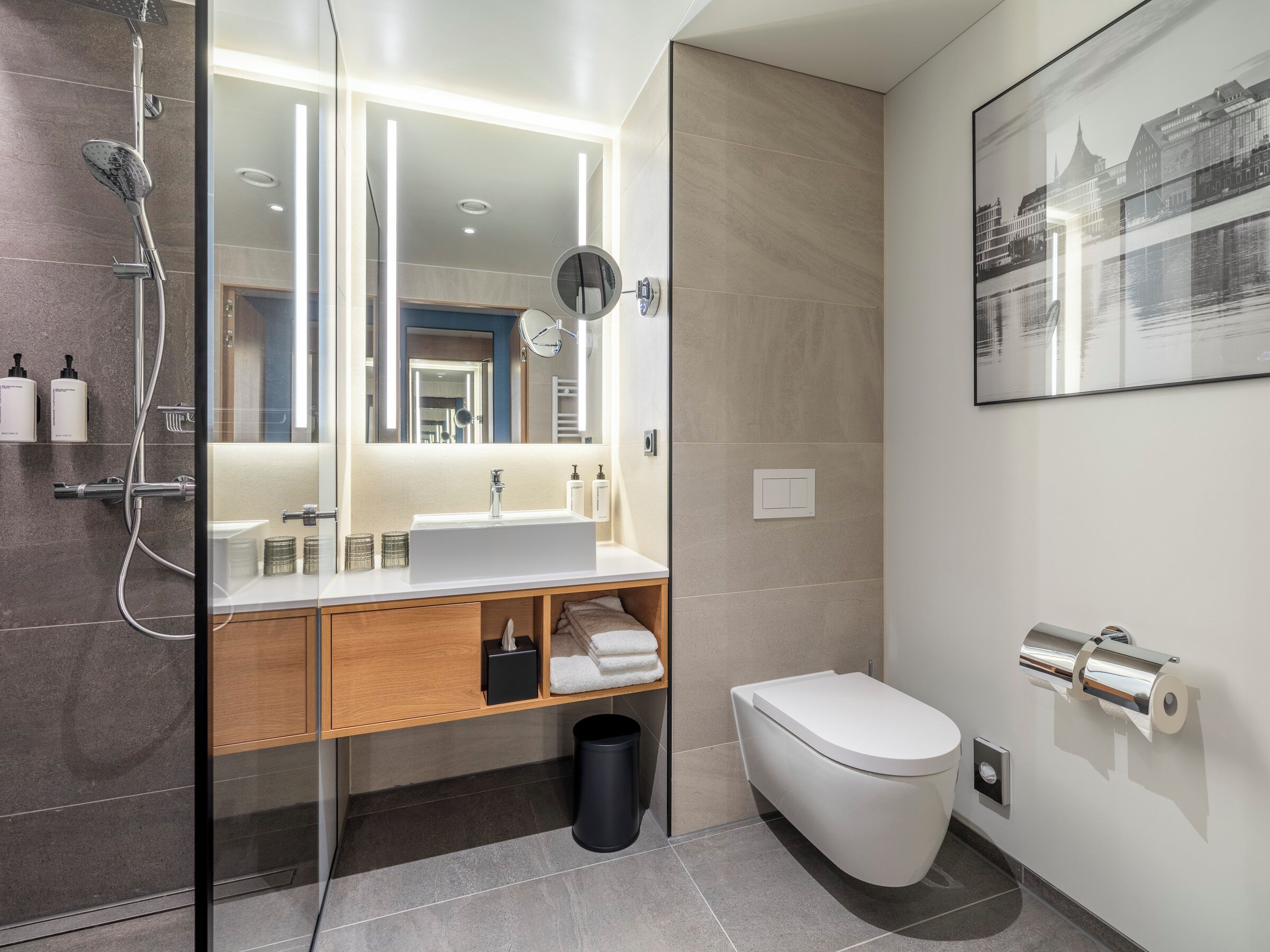 A modern bathroom with a glass-enclosed shower, a wooden vanity, a white sink, a mirror, a toilet, and a roll of toilet paper.