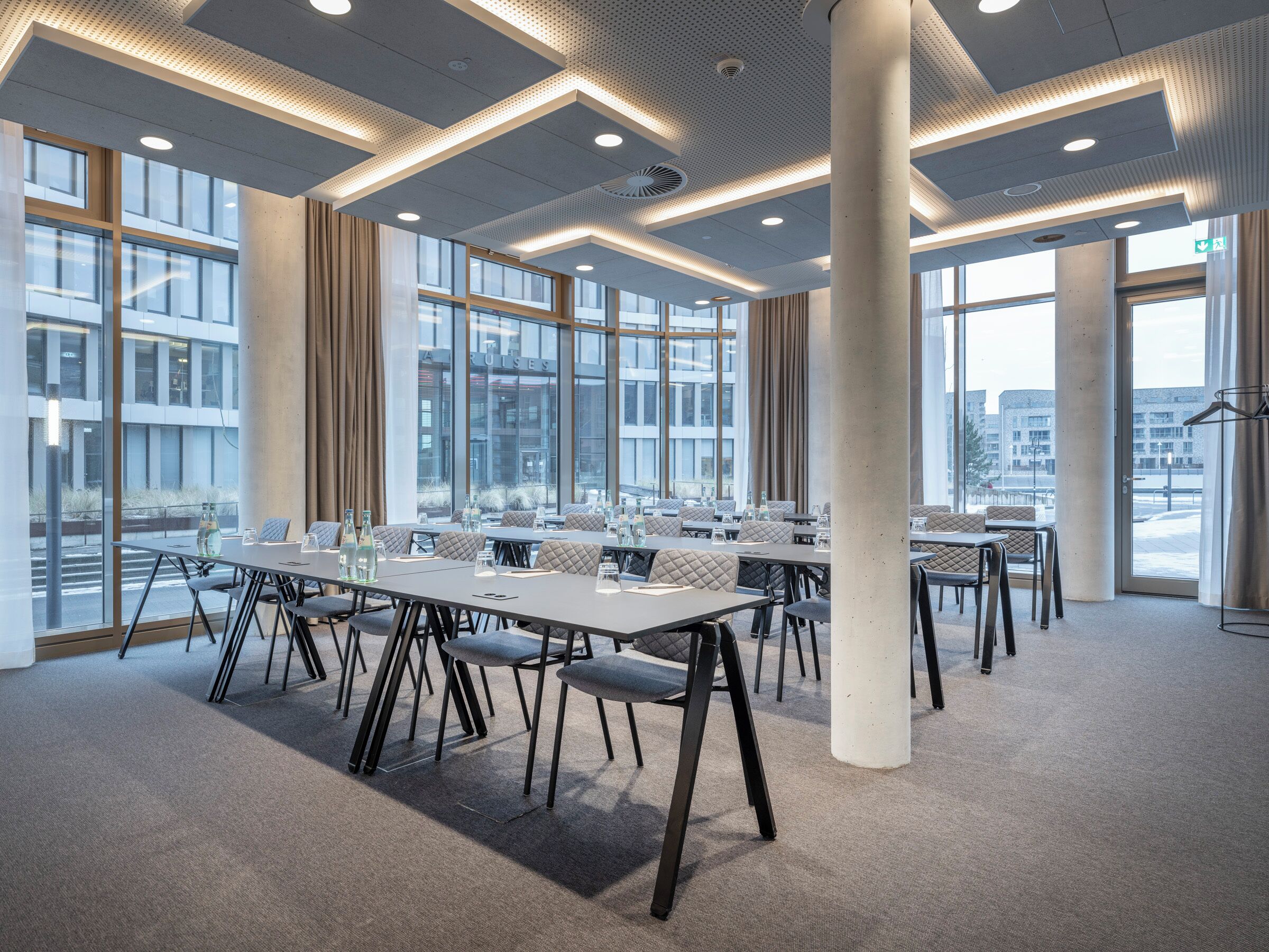 Un salón de conferencias con mesas grandes, sillas y un techo alto con iluminación empotrada.