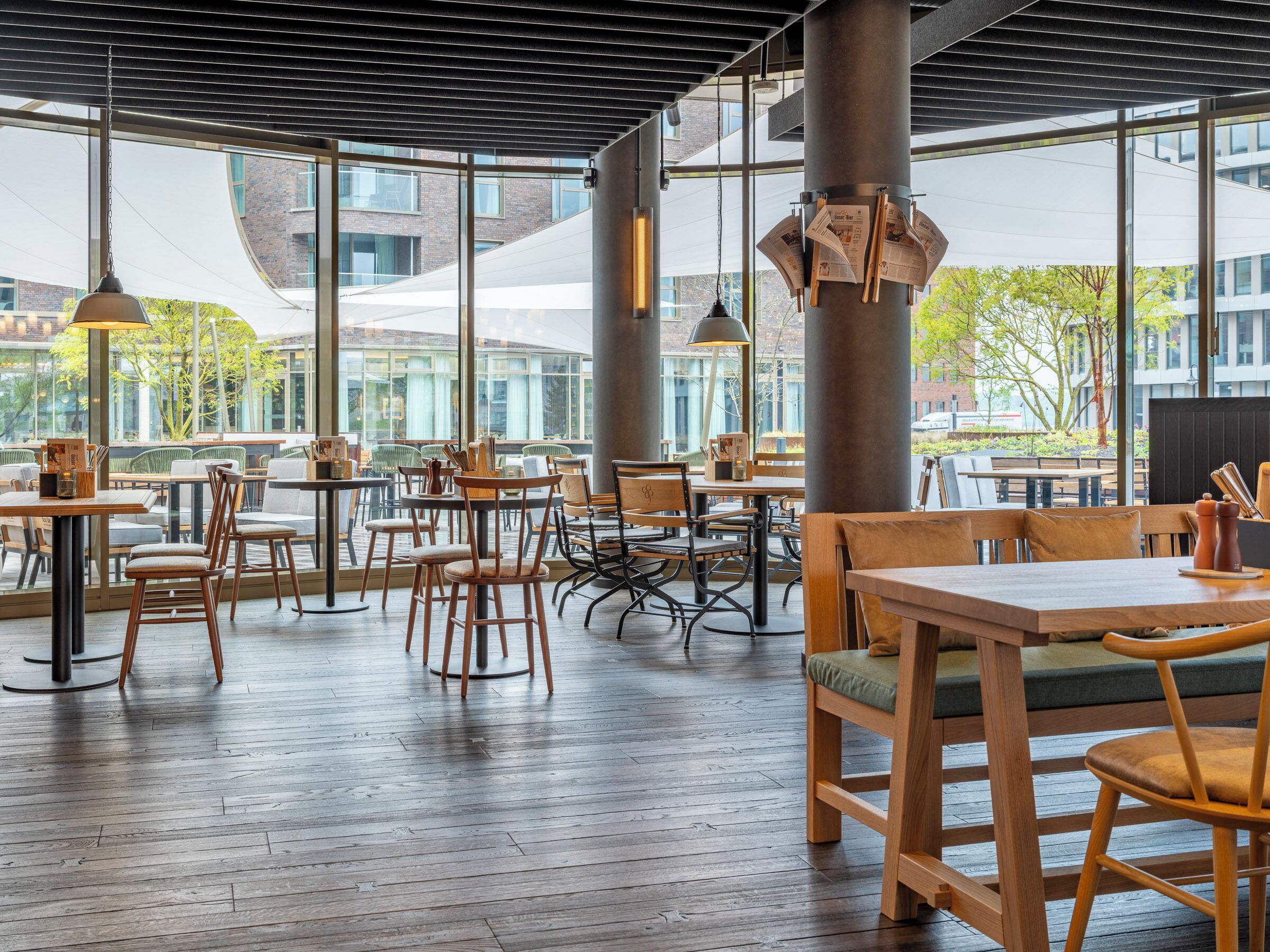An indoor dining area with wooden tables and chairs, large windows, and hanging pendant lights.