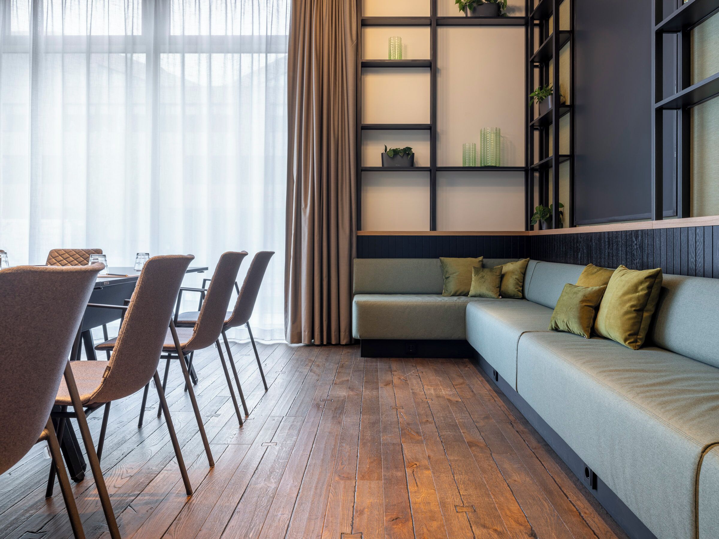 Un salon moderne avec un plancher en bois, un canapé gris agrémenté de coussins et un coin repas comprenant des chaises et une table.