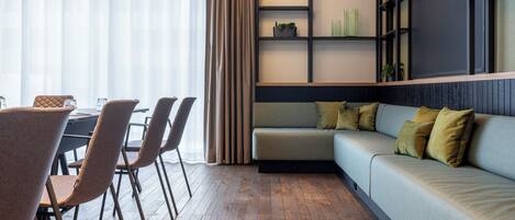 Un salon moderne avec un plancher en bois, un canapé gris agrémenté de coussins et un coin repas comprenant des chaises et une table.