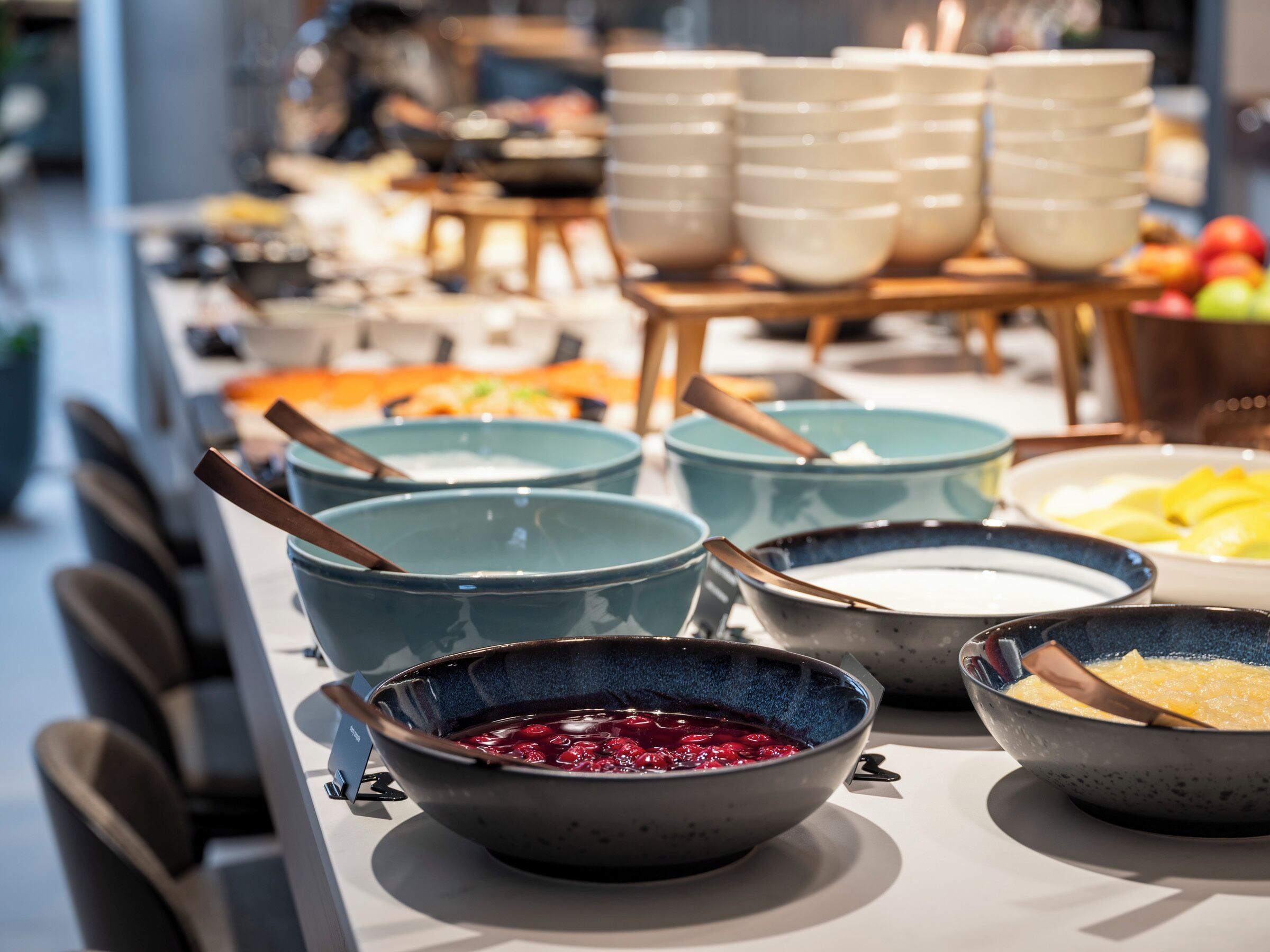 Een buffet tafel met diverse schalen eten, waaronder een schaal rode fruitcompote, een schaal yoghurt en een schaal roerei.