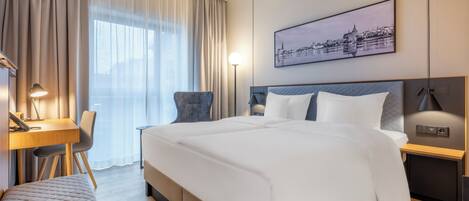Habitación de hotel moderna con una cama grande, un escritorio, una silla y vistas a un paisaje urbano a través de la ventana.