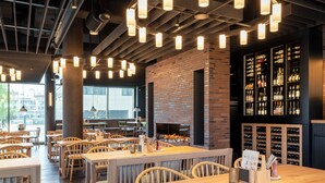 A restaurant interior with wooden tables and chairs, hanging pendant lights, a brick wall, and wine racks. - Scanhotels Stadthafen - Neueröffnung (Rostock)