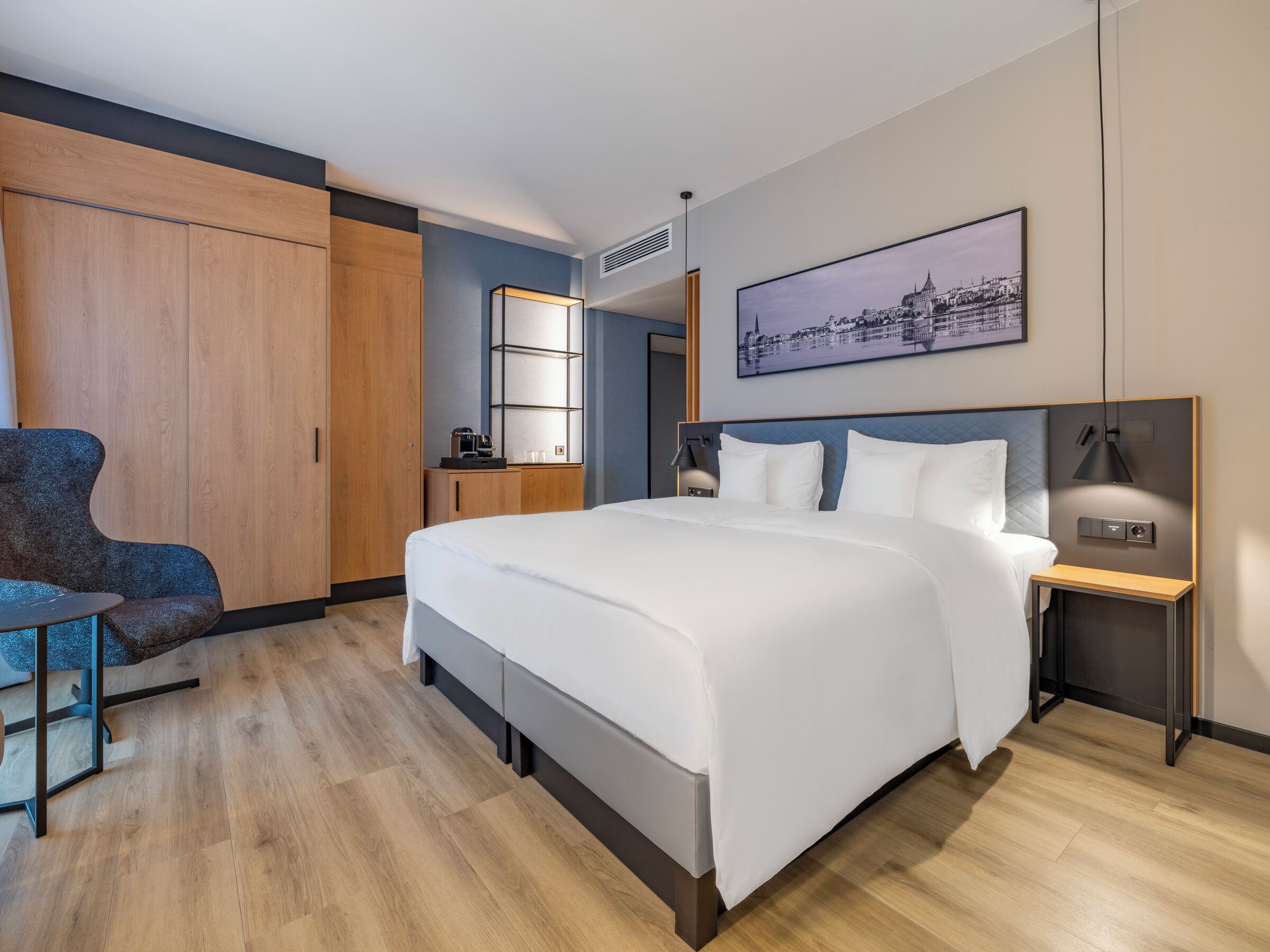 Een moderne hotelkamer met een groot bed, een fauteuil, een bureau en een stadsgezicht op de muur.