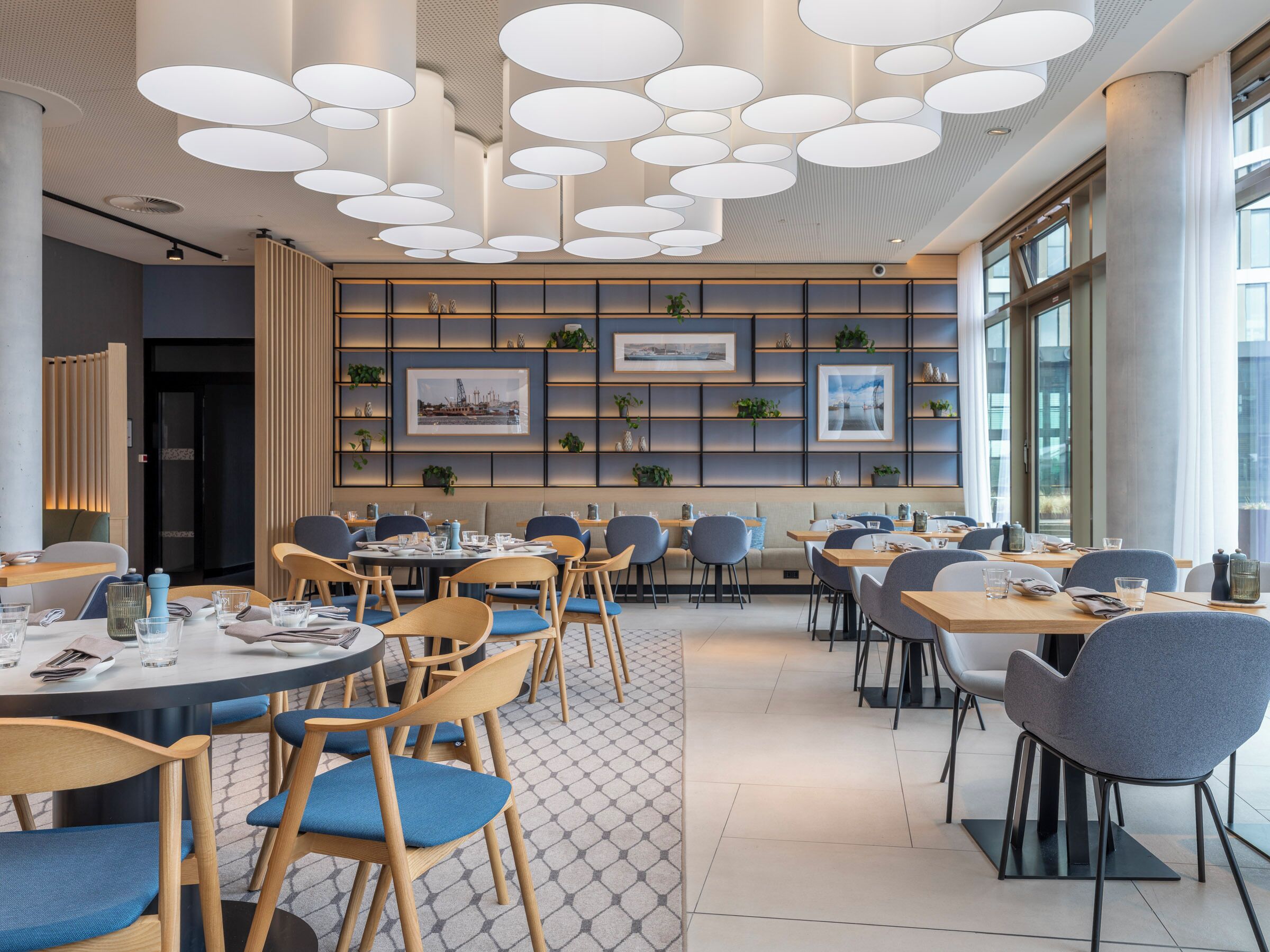 A modern dining area with round tables, chairs, and a ceiling with circular light fixtures.