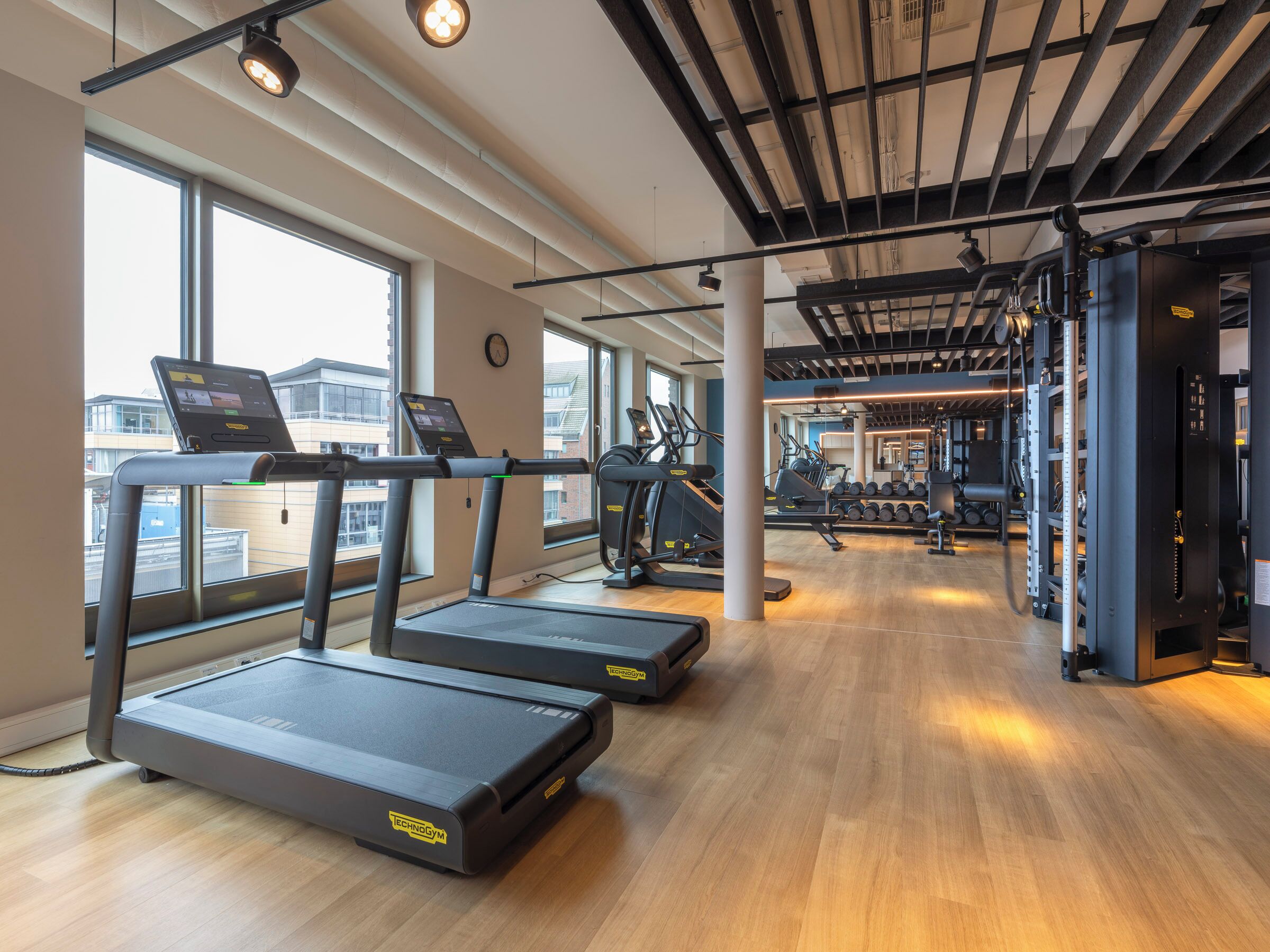 Une salle de sport équipée de tapis de course, d’appareils de musculation et dotée d’une grande fenêtre.