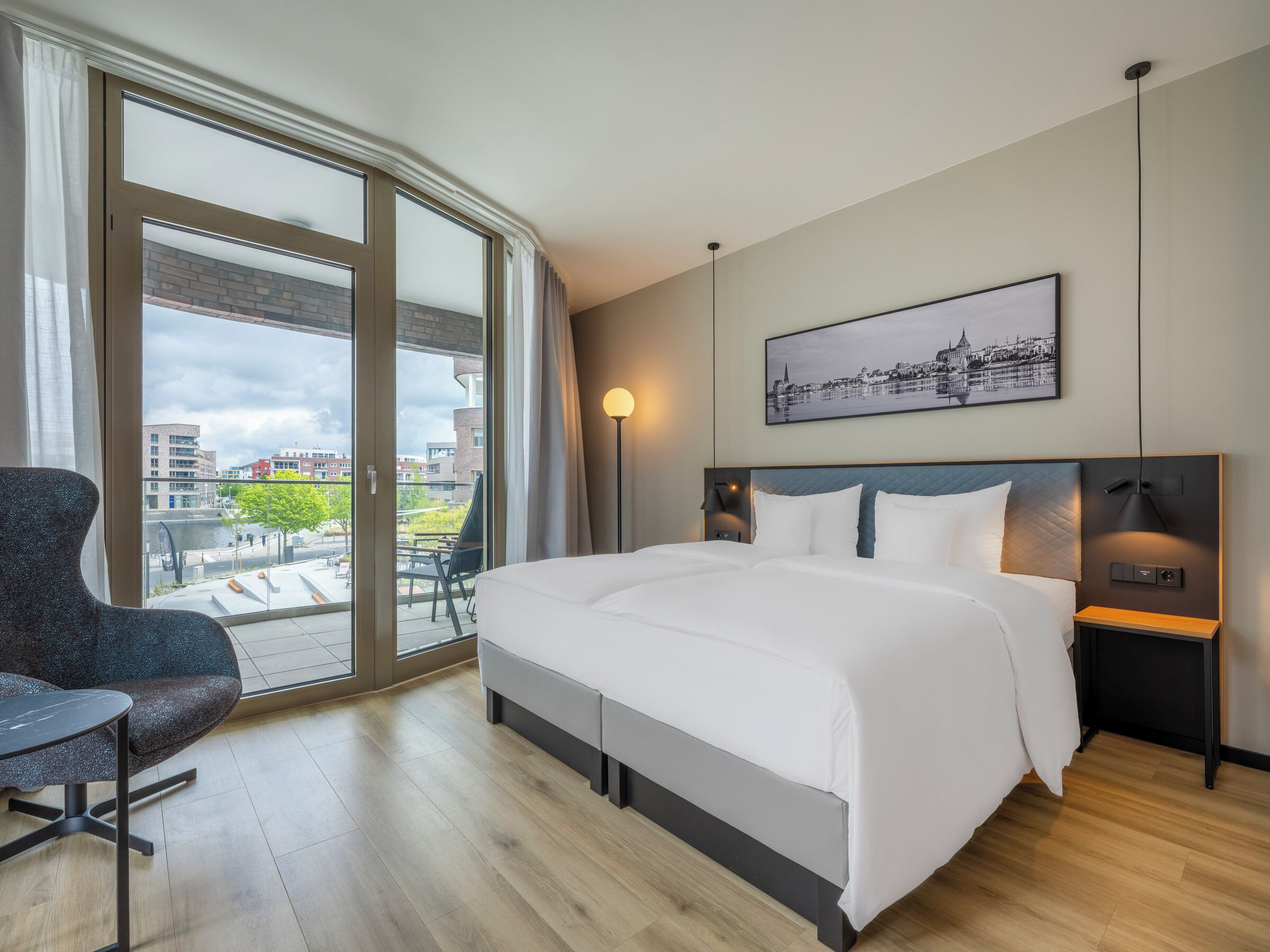Une chambre d’hôtel moderne, dotée d’un grand lit, d’un bureau, d’une chaise et offrant une vue sur le paysage urbain par la fenêtre.
