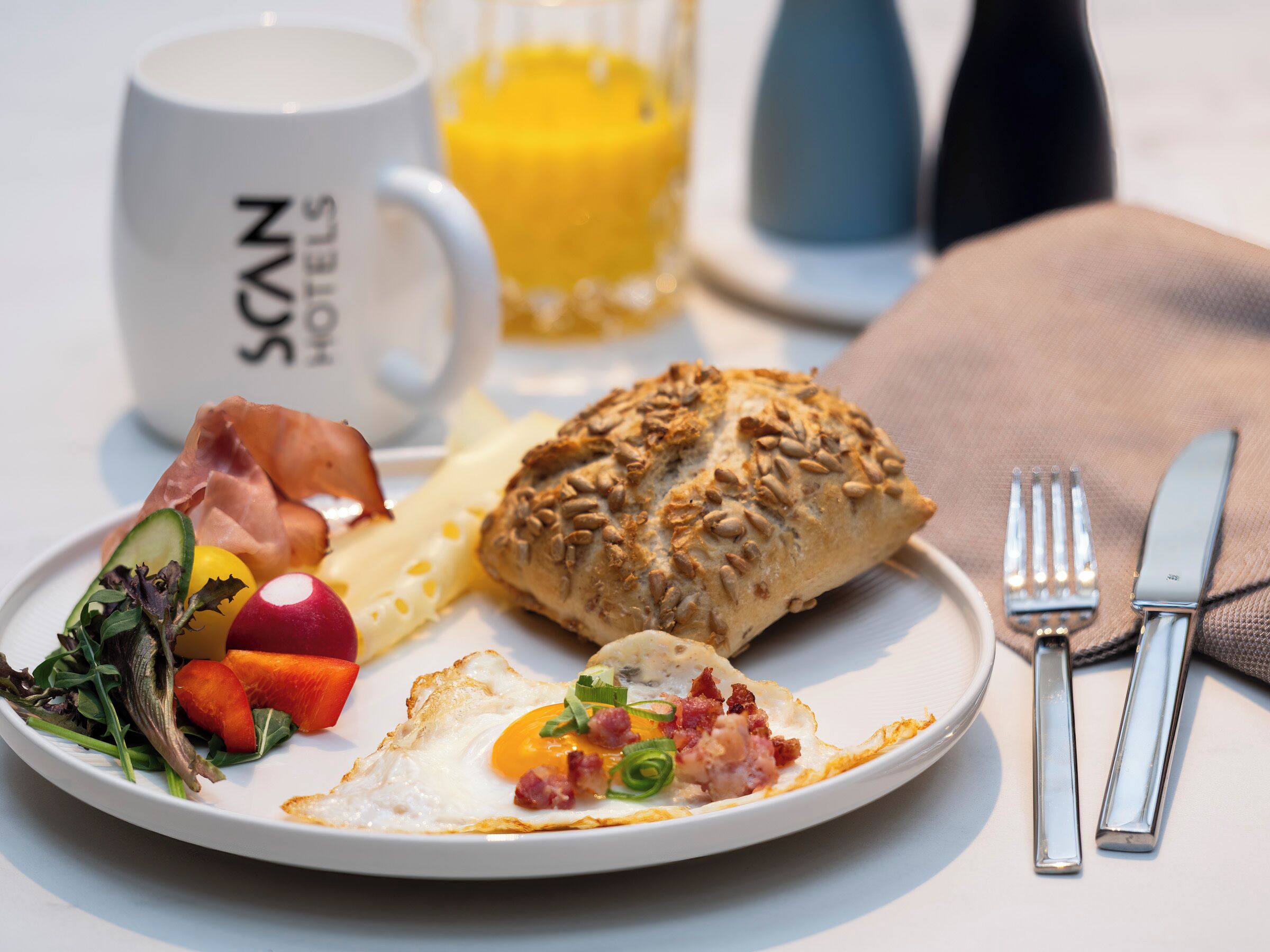 A breakfast plate with eggs, ham, vegetables, and a pastry, accompanied by a mug and a glass of orange juice.