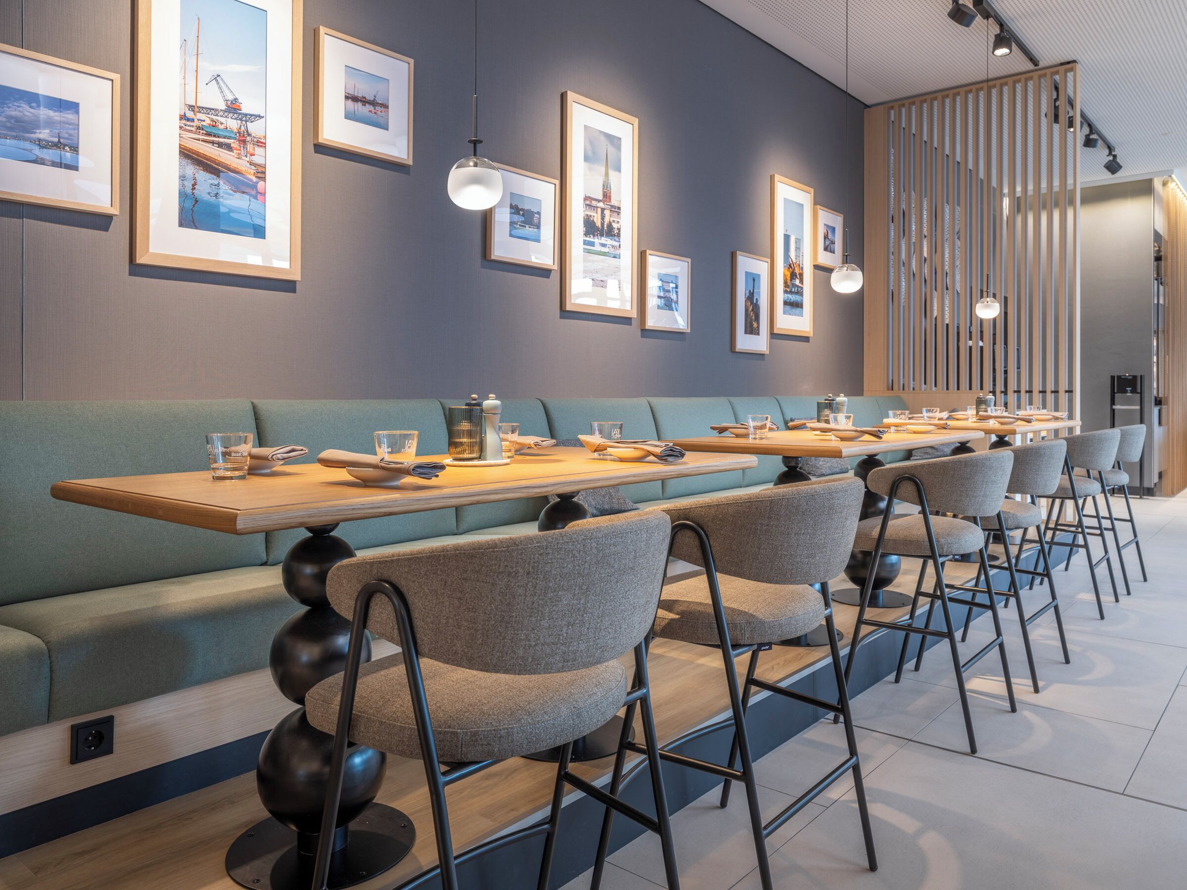 Un restaurant moderne avec un intérieur élégant, de longues tables conviviales, des sièges rembourrés et des tableaux encadrés accrochés aux murs.