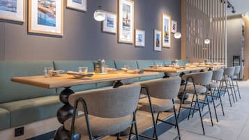 Un restaurant moderne avec un intérieur élégant, de longues tables conviviales, des sièges rembourrés et des tableaux encadrés accrochés aux murs.