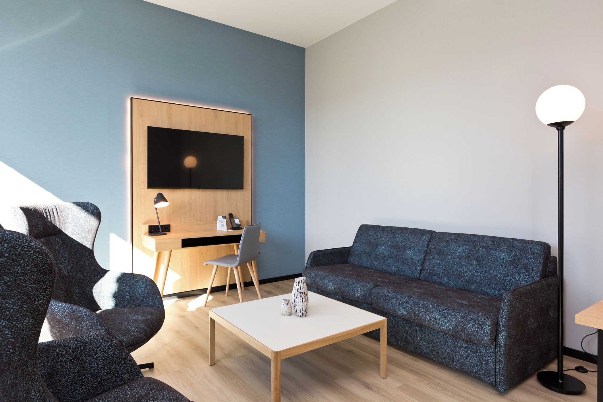 Un salon moderne comprenant un canapé, une table basse, un téléviseur fixé au mur et un bureau avec une chaise.