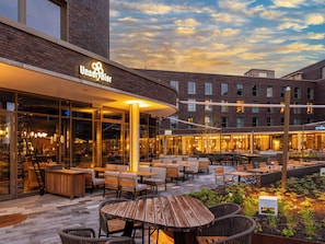 An outdoor seating area with tables and chairs, a brick building with a sign that reads 'UnserBier,' and a clear sky. - Scanhotels Stadthafen - Neueröffnung (Rostock)