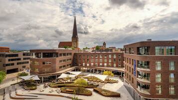 A modern building with a courtyard, a church spire, and a view of the sky.