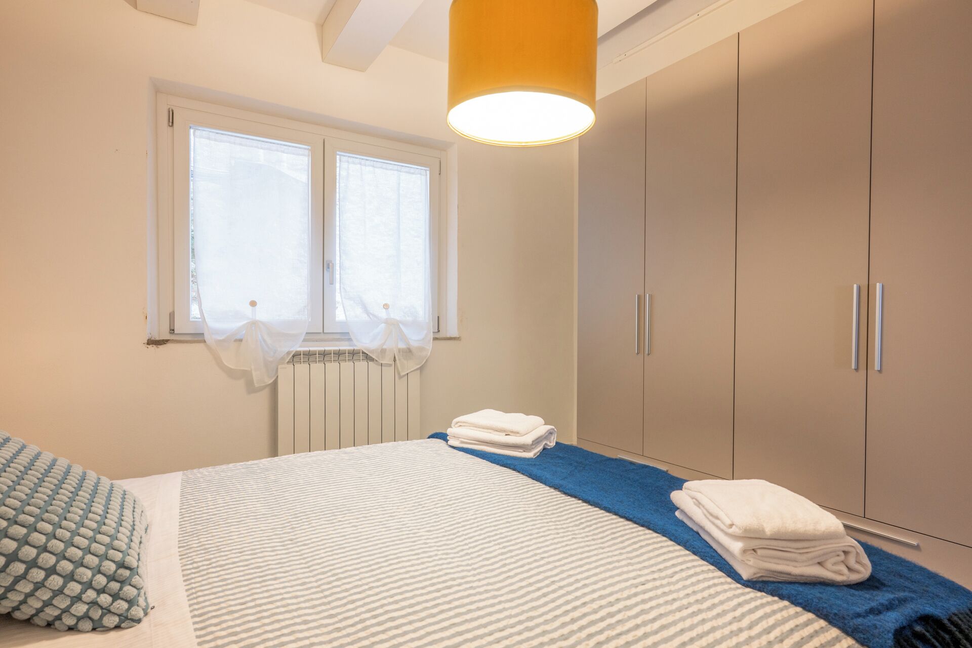 A bedroom with a bed, a radiator, a window with curtains, and a wardrobe.