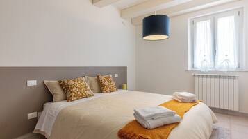 A bedroom with a bed, a bedside lamp, a window with curtains, and a radiator.