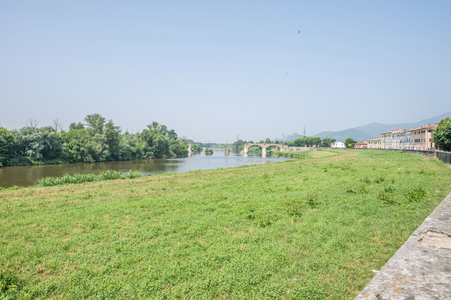 A river with a bridge, grassy banks, and buildings in the background.