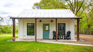 A small, single-story building with a white exterior and a blue door. It features two black Adirondack chairs and a small table on the front porch. - Charming 1-bedroom house with WiFi and AC in Cowpens (Cowpens)